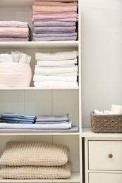 Photo of Home textile organization. Folded towels, bedsheets and pillows on shelving unit indoors