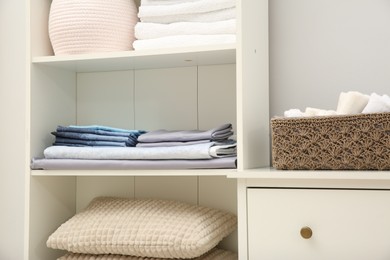 Photo of Home textile organization. Folded towels, bedsheets and pillows on shelving unit indoors, closeup