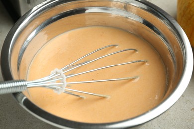 Photo of Bowl with dough for pumpkin pancakes and whisk on table, closeup