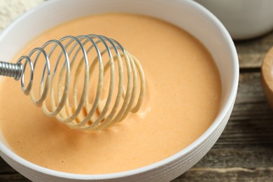 Photo of Bowl with dough for pumpkin pancakes and whisk on wooden table, closeup