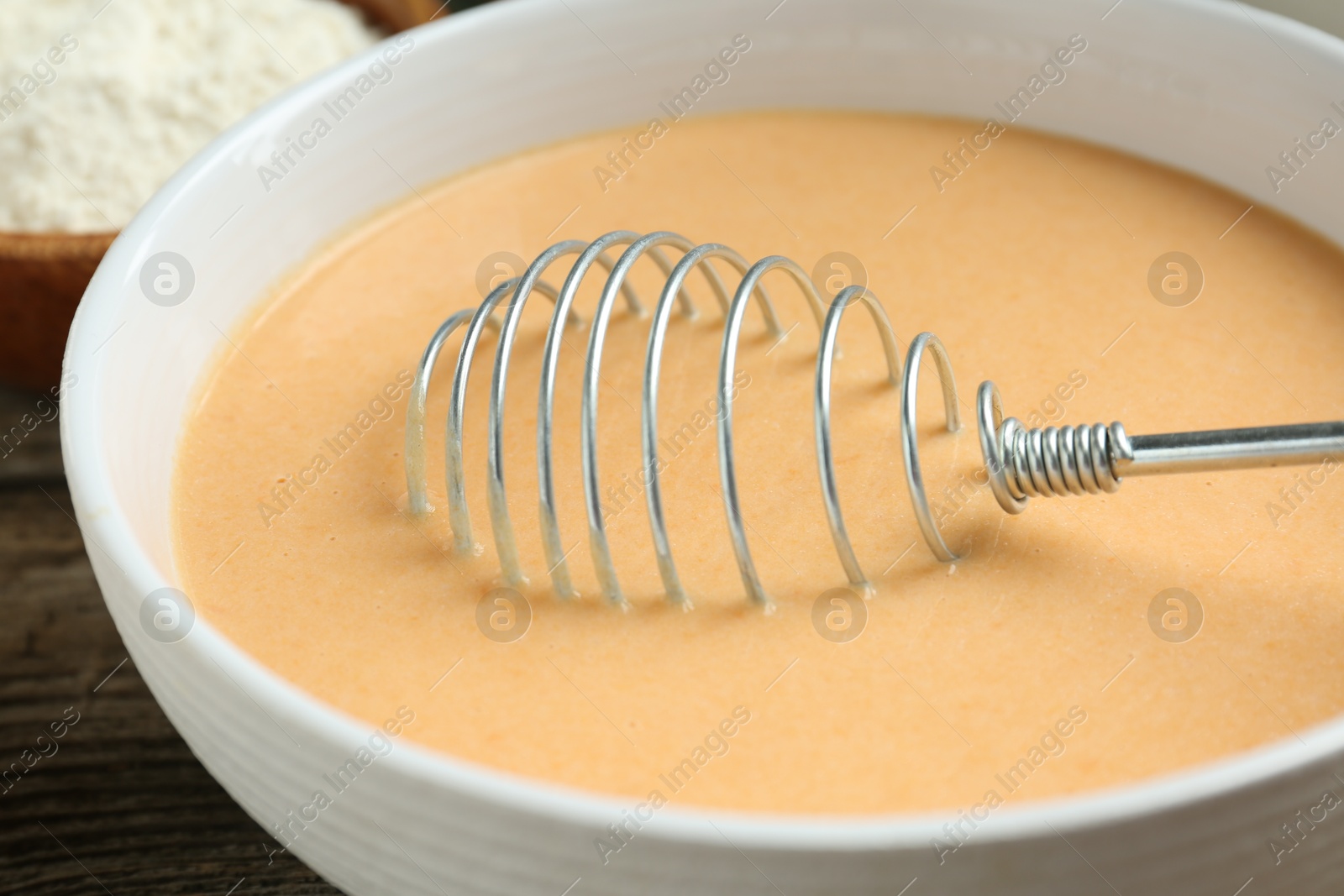 Photo of Bowl with dough for pumpkin pancakes and whisk on table, closeup