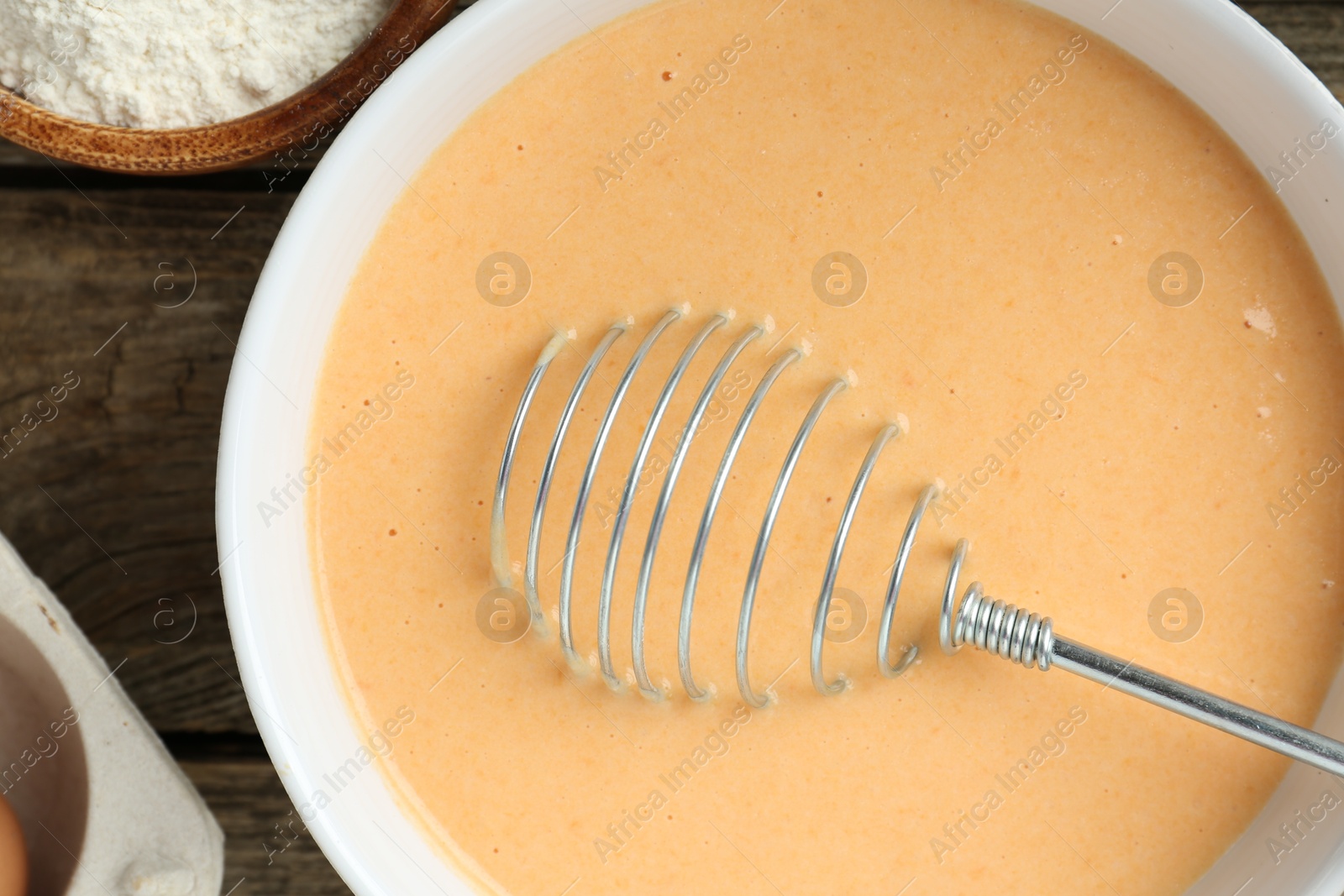 Photo of Bowl with dough for pumpkin pancakes and whisk on wooden table, closeup