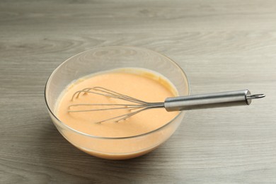 Photo of Bowl with dough for pumpkin pancakes and whisk on wooden table