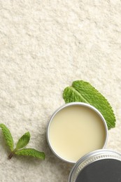 Photo of Mint lip balm and green leaves on beige textured background, top view. Space for text