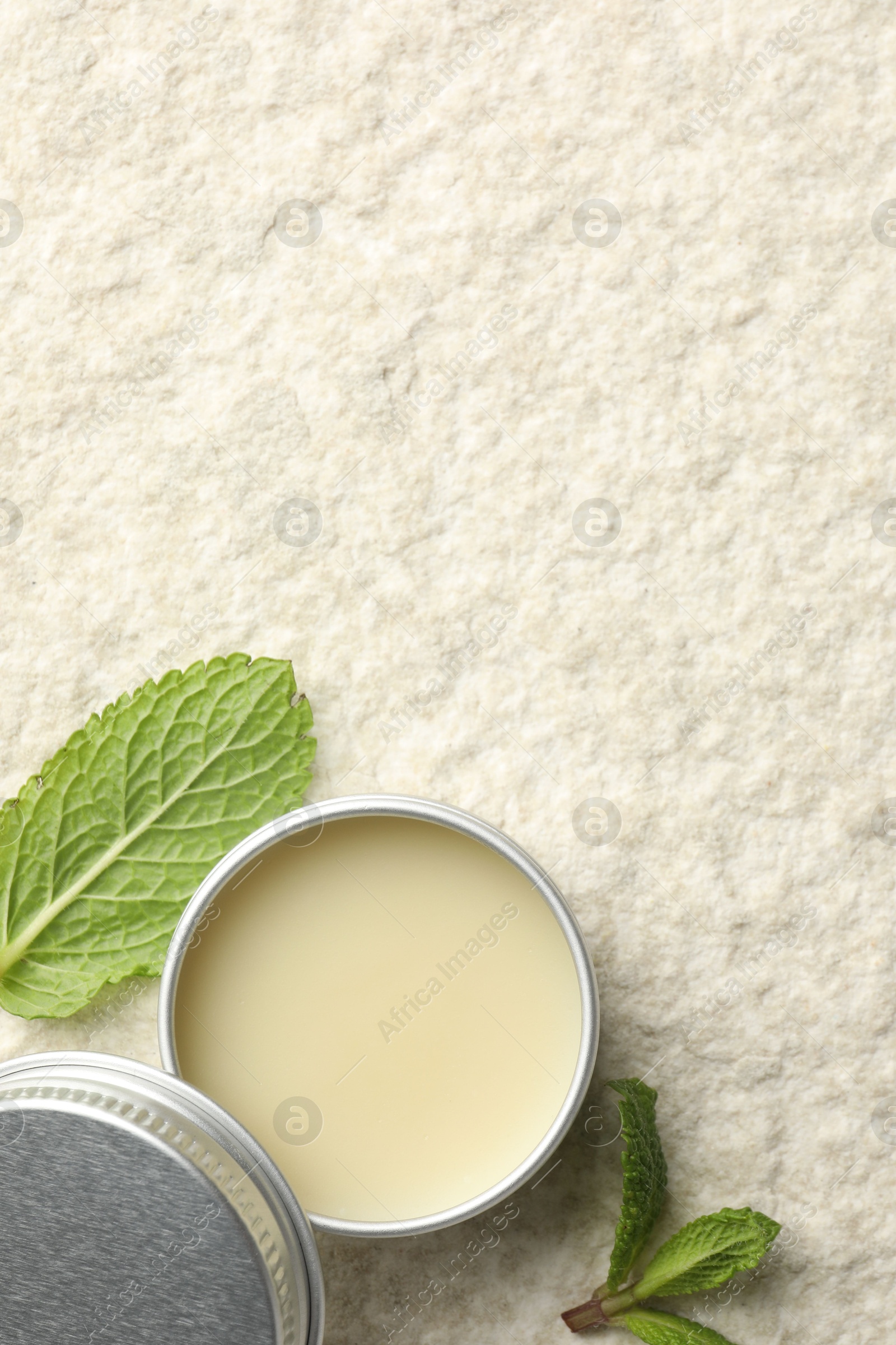 Photo of Mint lip balm and green leaves on beige textured background, top view. Space for text