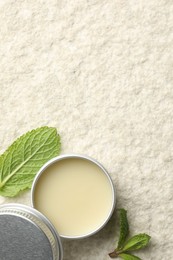 Photo of Mint lip balm and green leaves on beige textured background, top view. Space for text