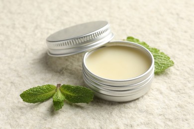 Photo of Mint lip balm and green leaves on beige textured table, closeup. Cosmetic product