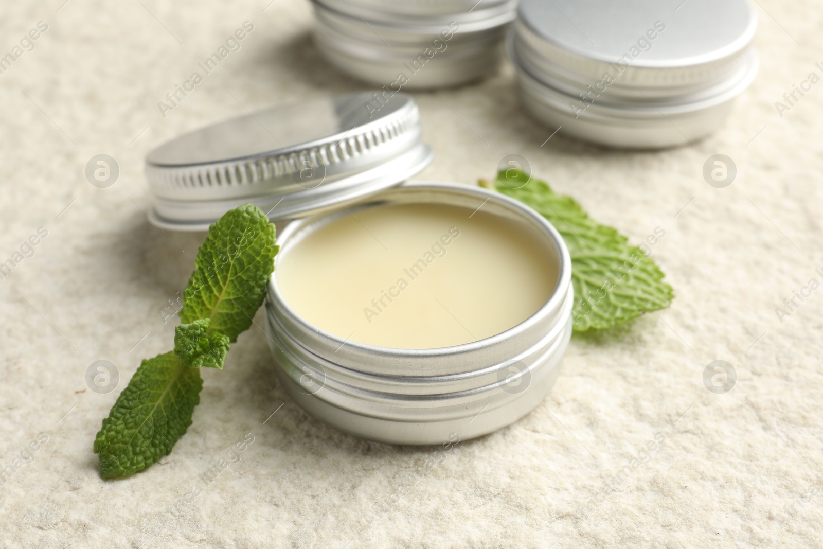 Photo of Mint lip balms and green leaves on beige textured table, closeup. Cosmetic product