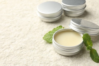 Photo of Mint lip balms and green leaves on beige textured table, closeup. Space for text