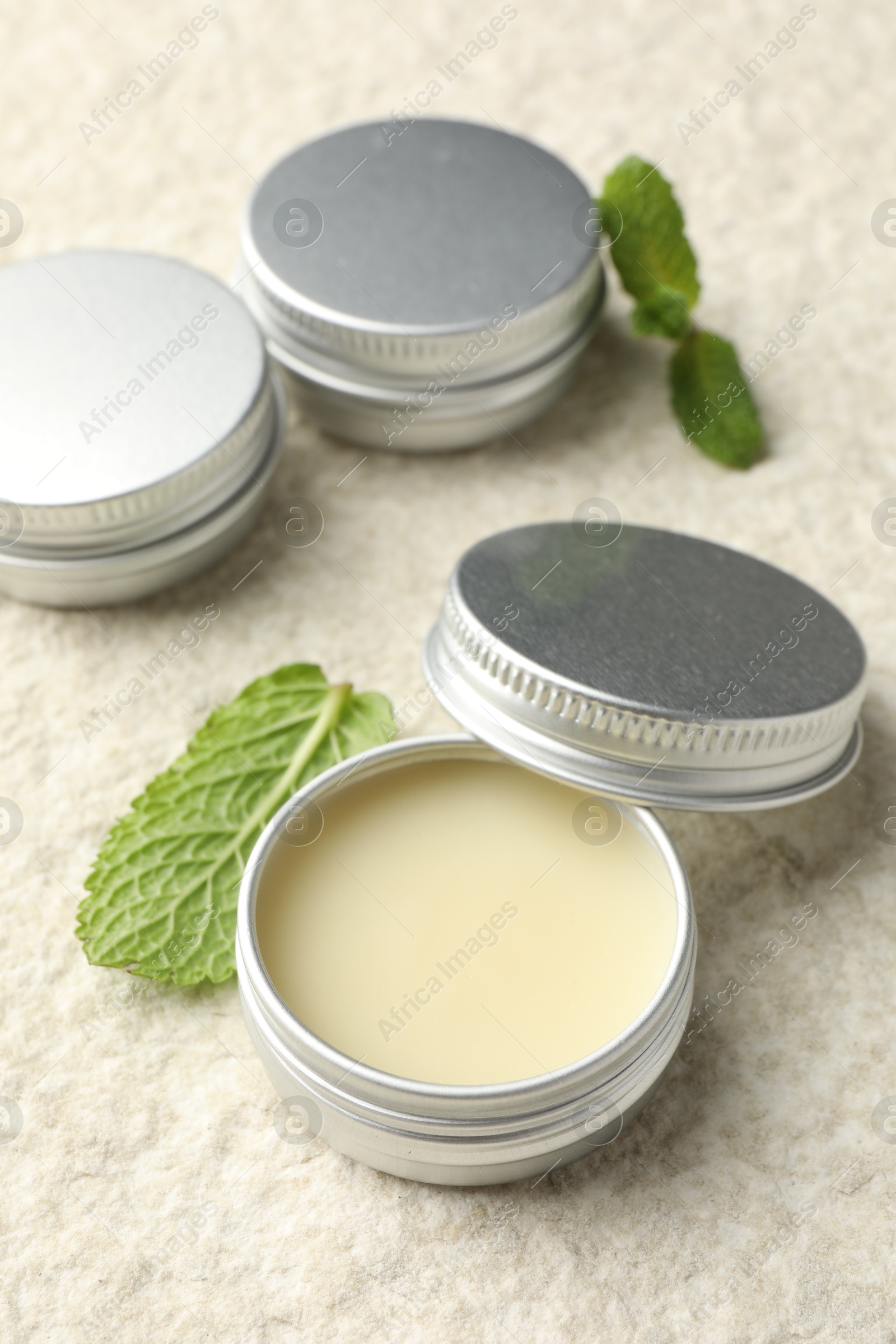 Photo of Mint lip balms and green leaves on beige textured table, closeup. Cosmetic product