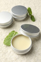 Photo of Mint lip balms and green leaves on beige textured table, closeup. Cosmetic product