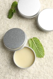 Photo of Mint lip balms and green leaves on beige textured background, flat lay. Cosmetic product