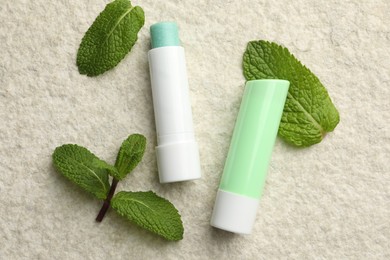 Photo of Mint lip balms and green leaves on beige textured table, flat lay. Cosmetic product