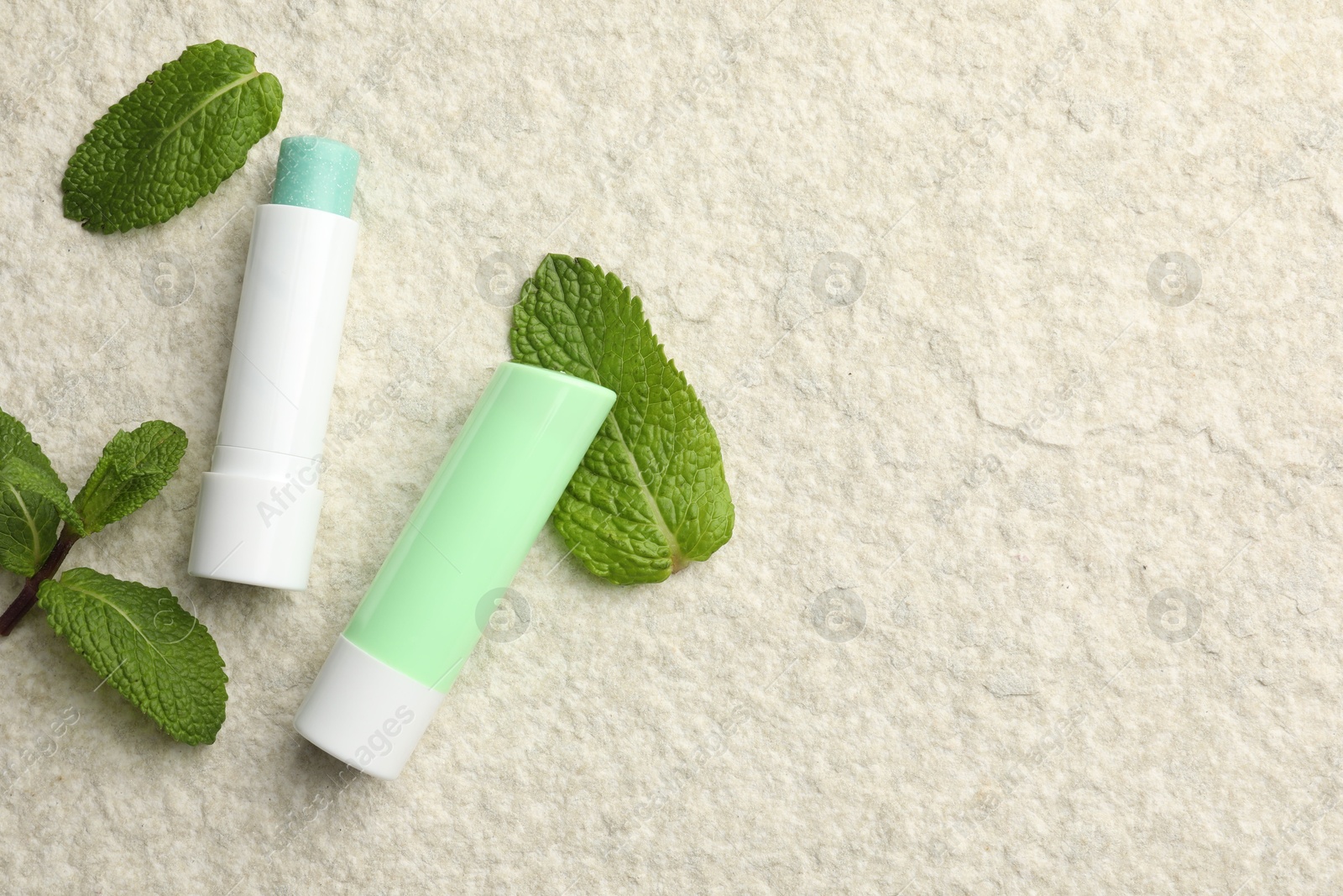 Photo of Mint lip balms and green leaves on beige textured background, flat lay. Space for text