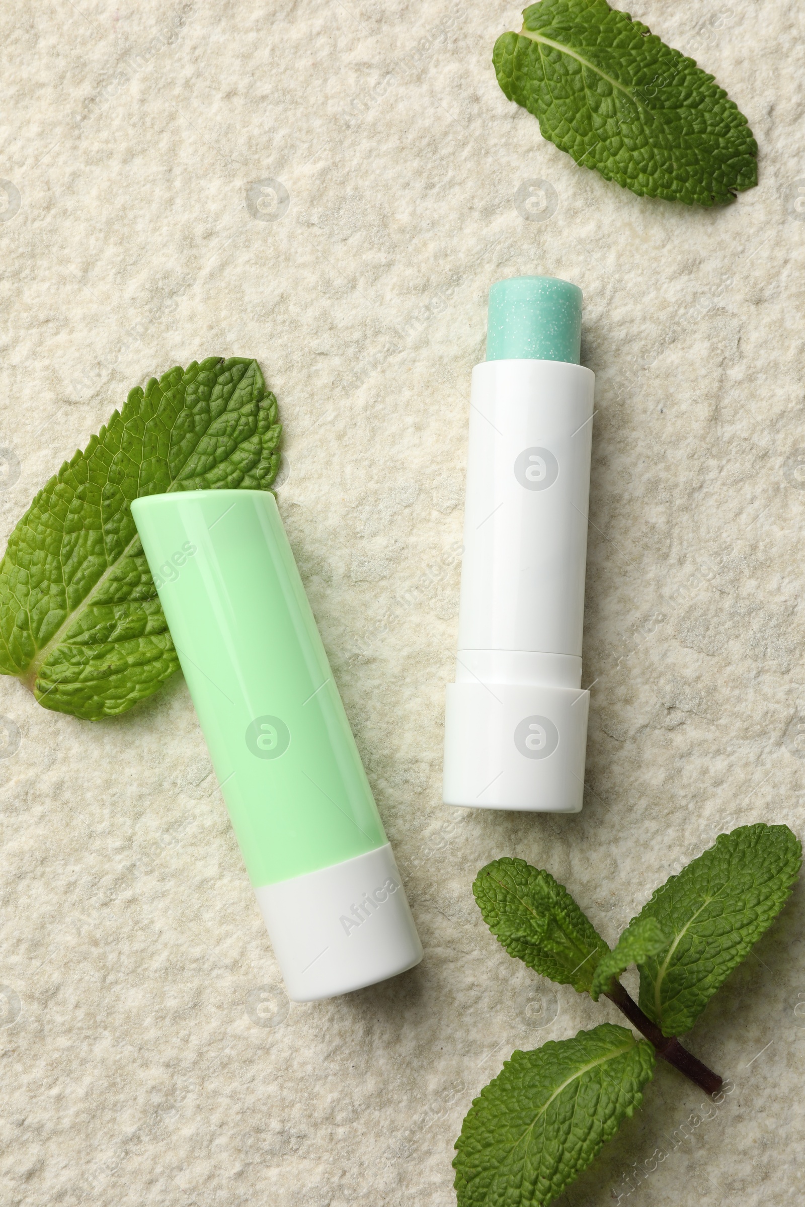 Photo of Mint lip balms and green leaves on beige textured table, flat lay. Cosmetic product