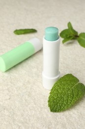 Photo of Mint lip balms and green leaves on beige textured table, closeup. Cosmetic product