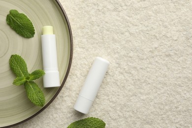 Photo of Mint lip balms and green leaves on beige textured background, top view. Space for text