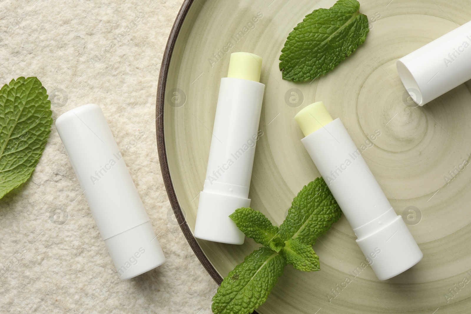 Photo of Mint lip balms and green leaves on beige textured background, top view. Cosmetic product