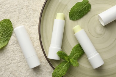 Photo of Mint lip balms and green leaves on beige textured background, top view. Cosmetic product