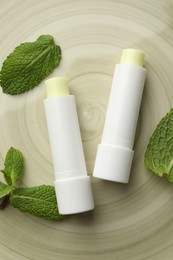 Photo of Mint lip balms and green leaves on plate, flat lay. Cosmetic product