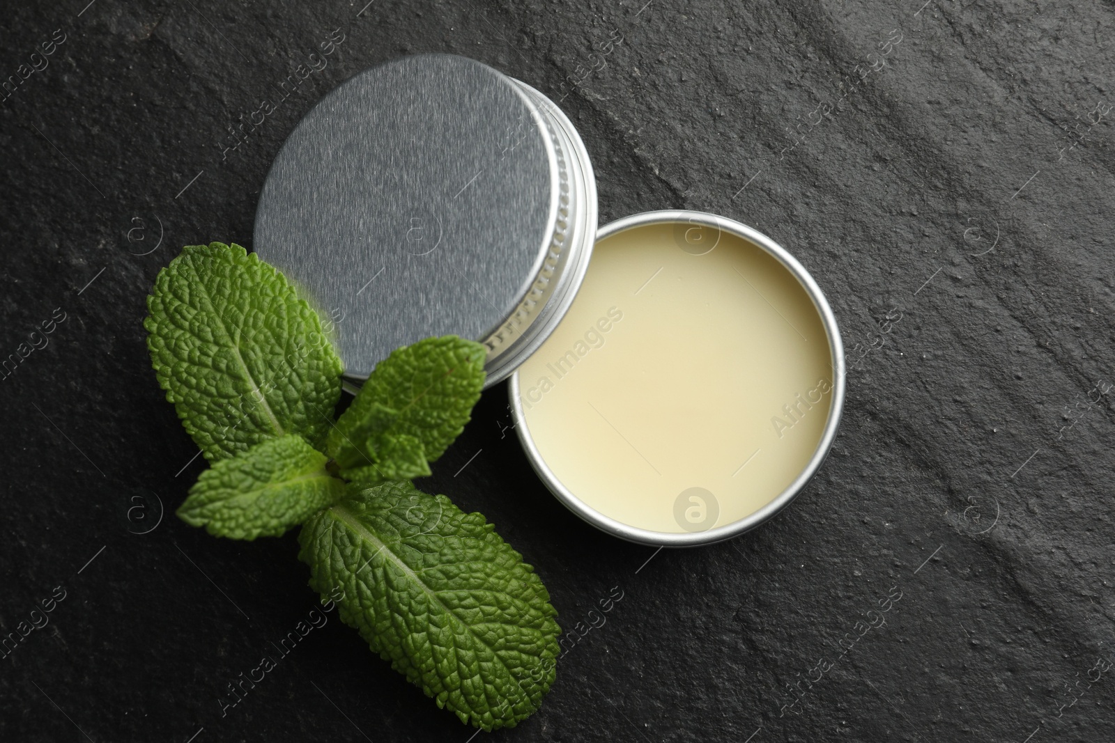 Photo of Mint lip balm and green leaves on black table, top view. Cosmetic product