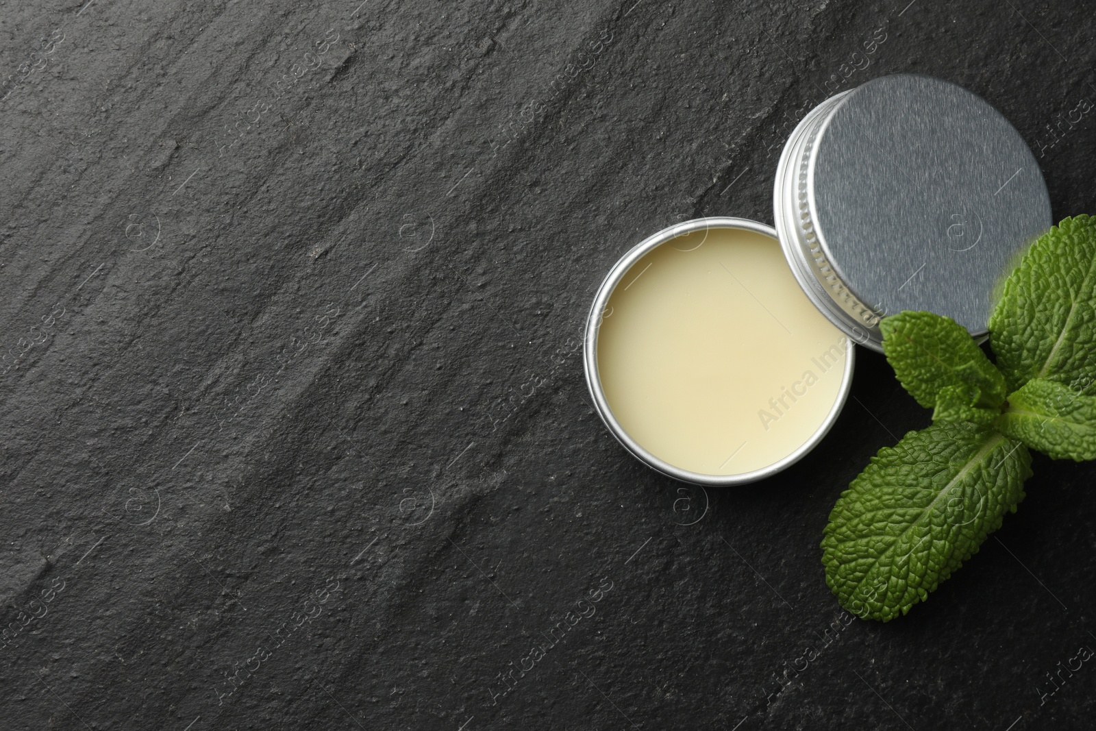 Photo of Mint lip balm and green leaves on black background, top view. Space for text