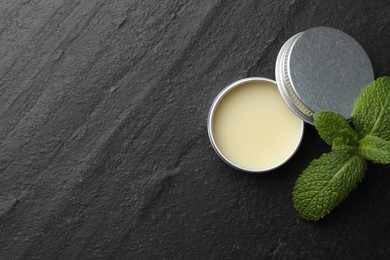 Photo of Mint lip balm and green leaves on black background, top view. Space for text