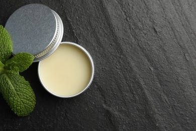 Photo of Mint lip balm and green leaves on black background, top view. Space for text