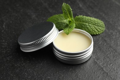 Photo of Mint lip balm and green leaves on black table, closeup. Cosmetic product