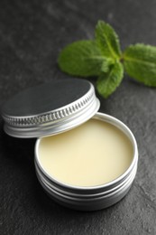 Photo of Mint lip balm and green leaves on black table, closeup. Cosmetic product