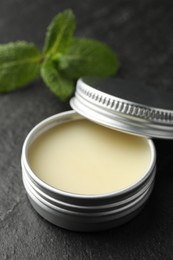 Photo of Mint lip balm and green leaves on black table, closeup. Cosmetic product