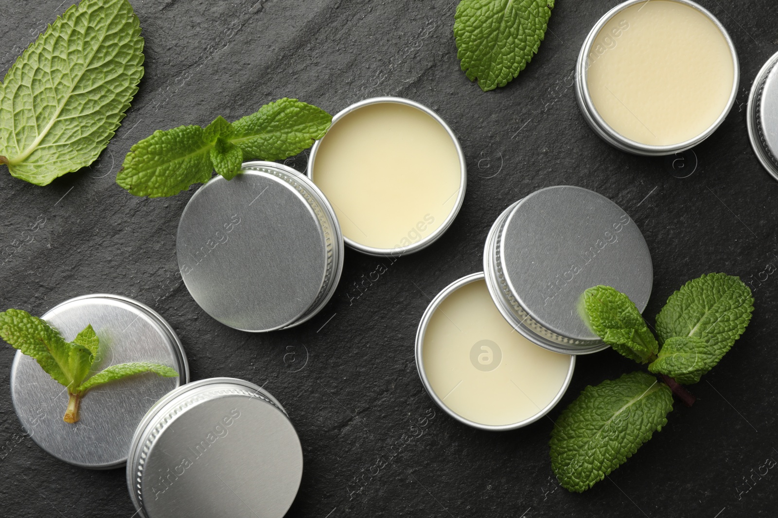 Photo of Mint lip balms and green leaves on black background, flat lay. Cosmetic product