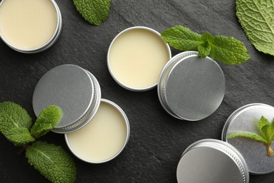 Photo of Mint lip balms and green leaves on black background, flat lay. Cosmetic product