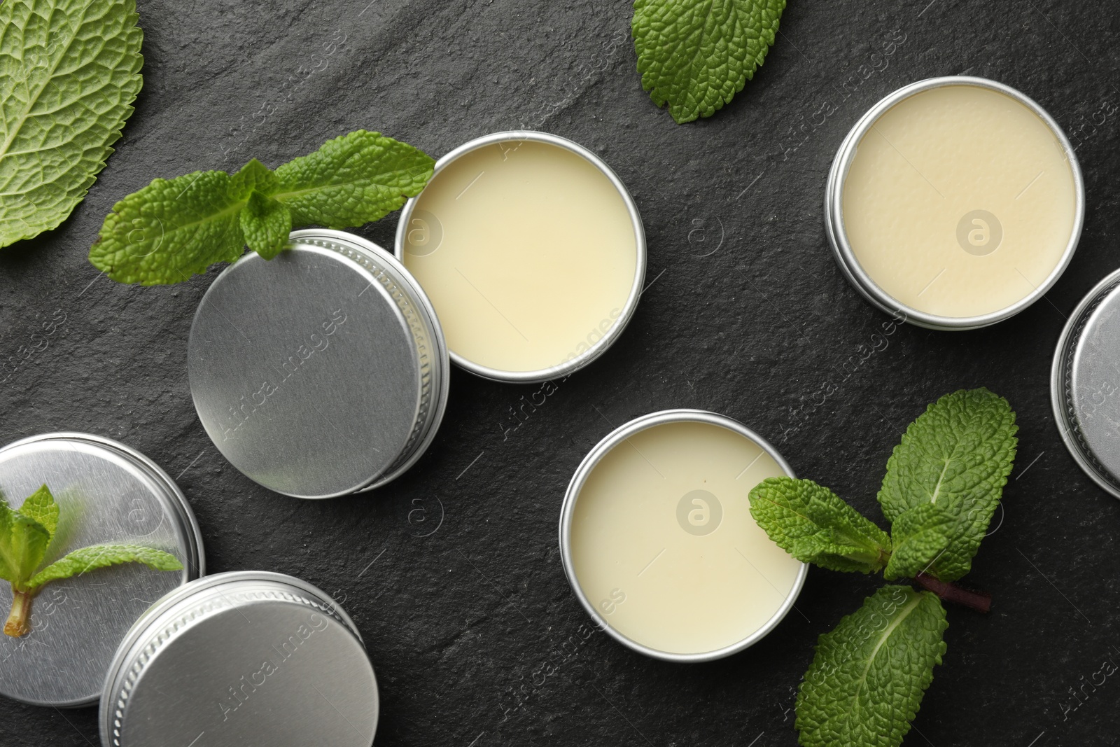 Photo of Mint lip balms and green leaves on black background, flat lay. Cosmetic product