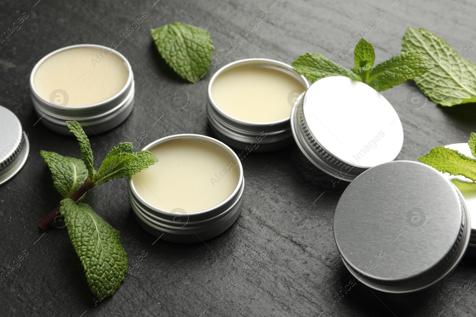 Photo of Mint lip balms and green leaves on black table, closeup. Cosmetic product