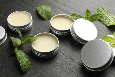 Photo of Mint lip balms and green leaves on black table, closeup. Cosmetic product