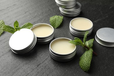 Photo of Mint lip balms and green leaves on black table, closeup. Cosmetic product