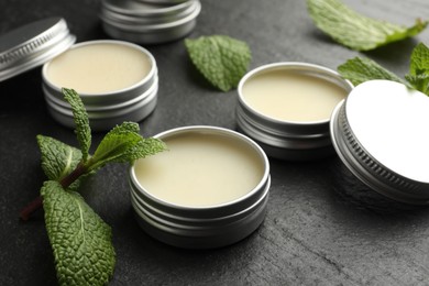 Photo of Mint lip balms and green leaves on black table, closeup. Cosmetic product