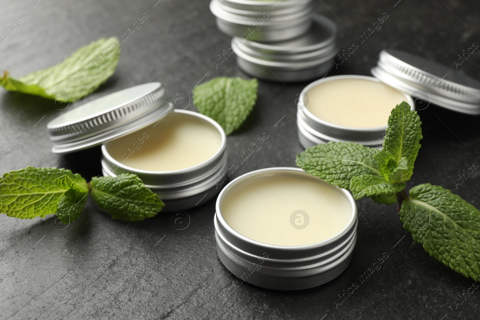 Photo of Mint lip balms and green leaves on black table, closeup. Cosmetic product