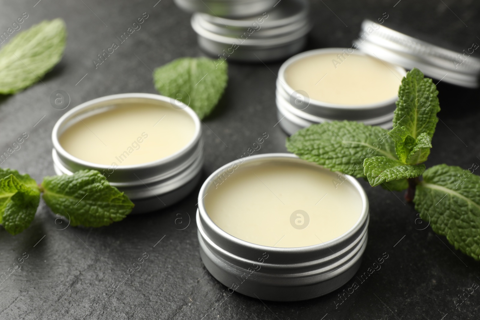 Photo of Mint lip balms and green leaves on black table, closeup. Cosmetic product