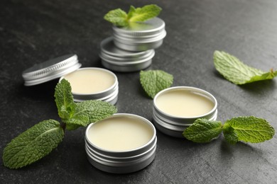 Photo of Mint lip balms and green leaves on black table, closeup. Cosmetic product