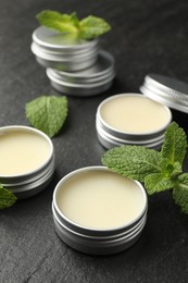 Photo of Mint lip balms and green leaves on black table, closeup. Cosmetic product