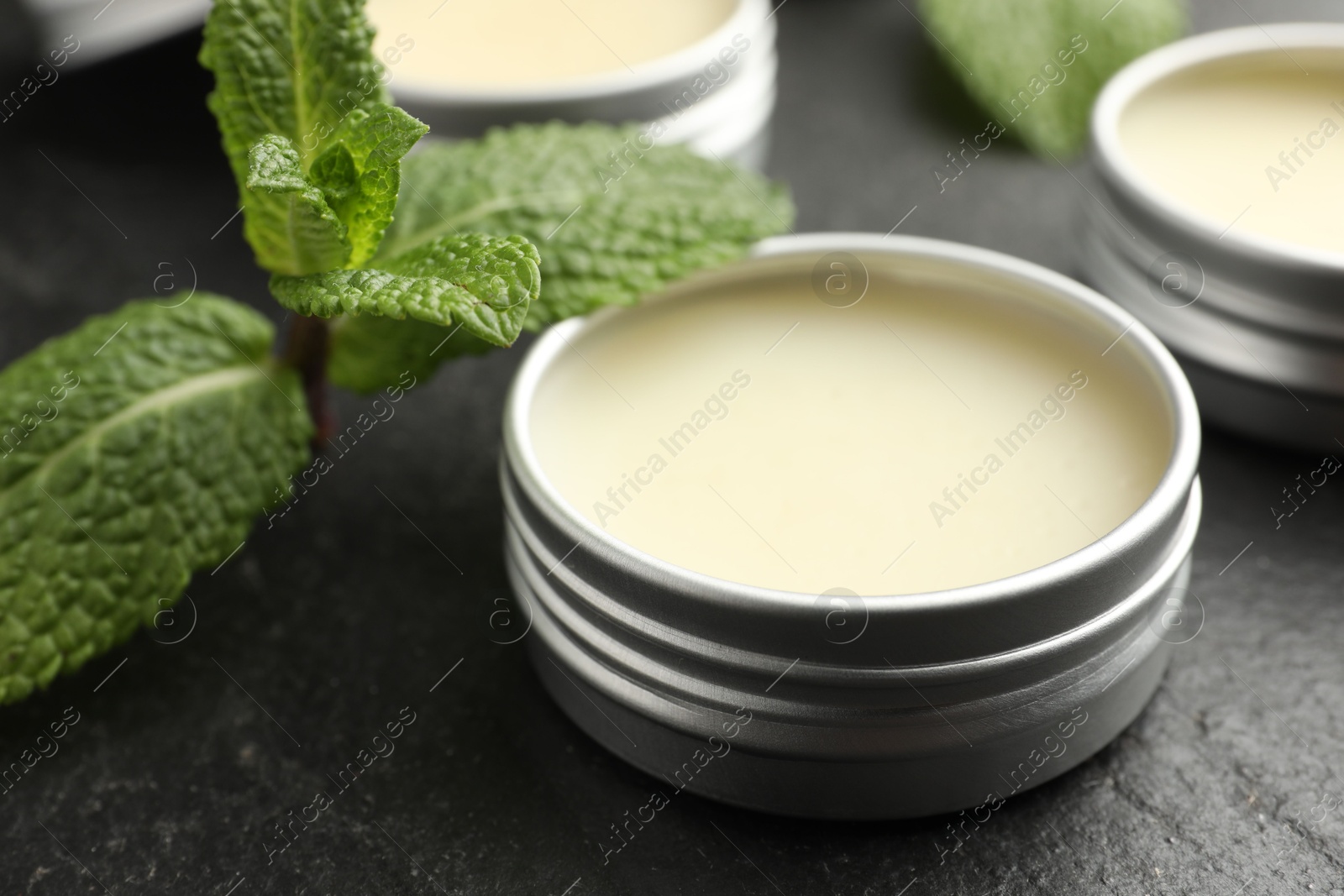 Photo of Mint lip balms and green leaves on black table, closeup. Cosmetic product