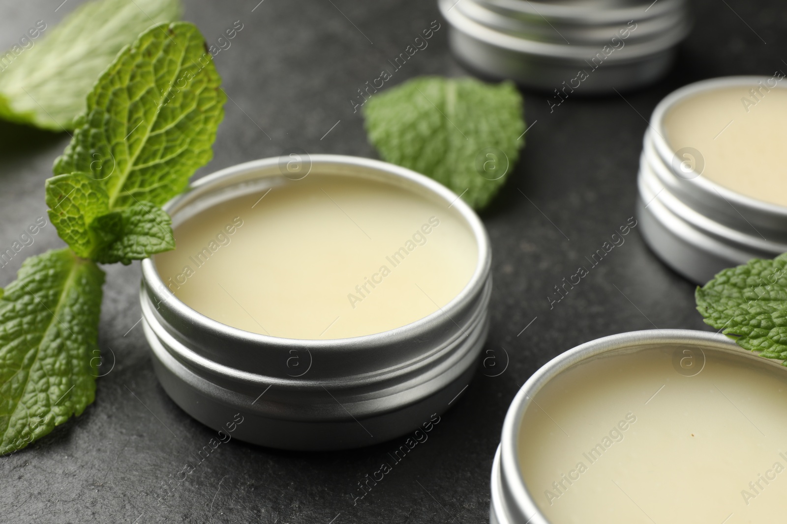 Photo of Mint lip balms and green leaves on black table, closeup. Cosmetic product