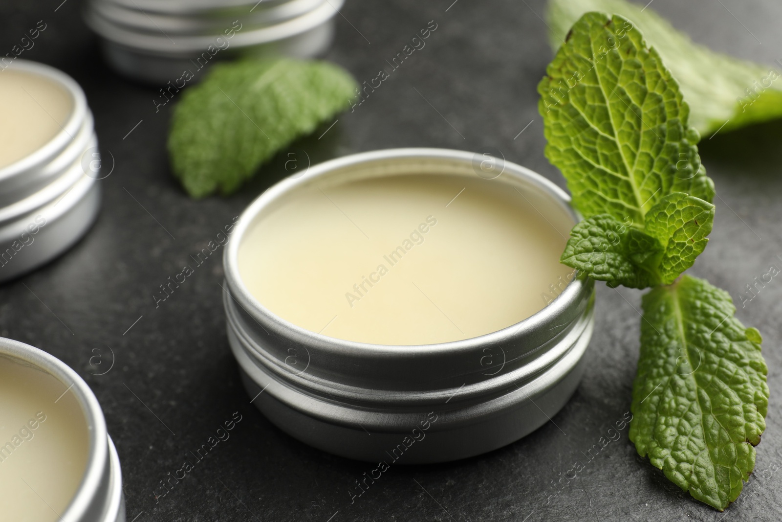 Photo of Mint lip balms and green leaves on black table, closeup. Cosmetic product