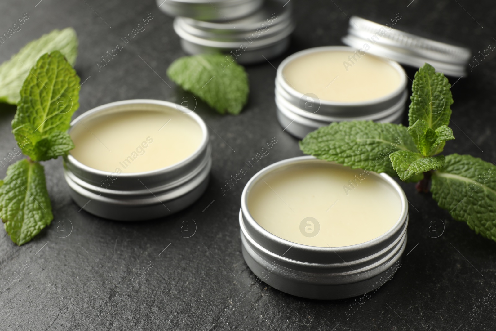 Photo of Mint lip balms and green leaves on black table, closeup. Cosmetic product