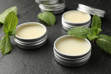 Photo of Mint lip balms and green leaves on black table, closeup. Cosmetic product