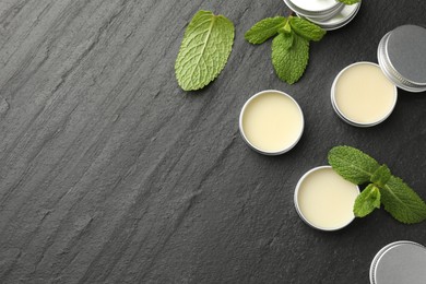 Photo of Mint lip balms and green leaves on black background, flat lay. Space for text