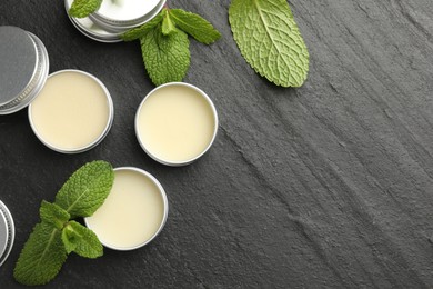 Photo of Mint lip balms and green leaves on black background, flat lay. Space for text