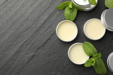 Photo of Mint lip balms and green leaves on black background, flat lay. Space for text